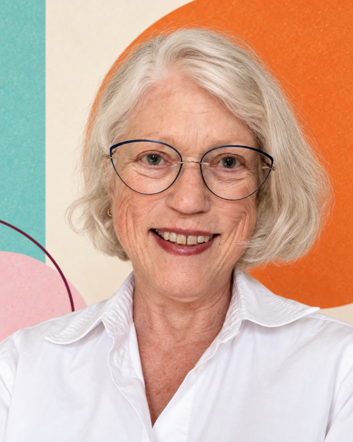 Judith Sullivan smiling, against a colorful geometric background
